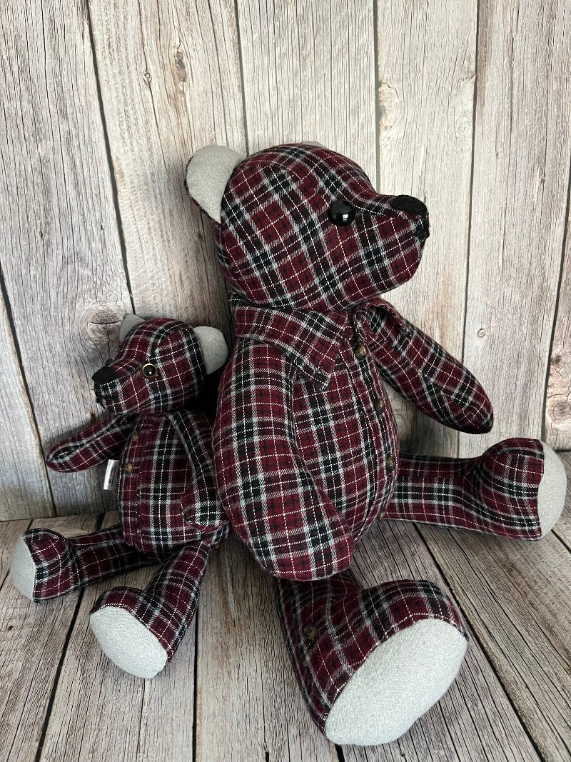 An 8 inch mini bear is sitting back to back with a 12 inch memory bear. The bears are made from a burgandy and black plaid shirt.
