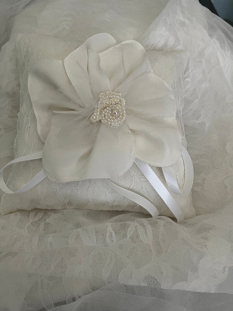 8x8 ivory ring bearer pillow made from an repurposed wedding gown. The pillow is covered with ivory lace and has a large flower sewn on top.