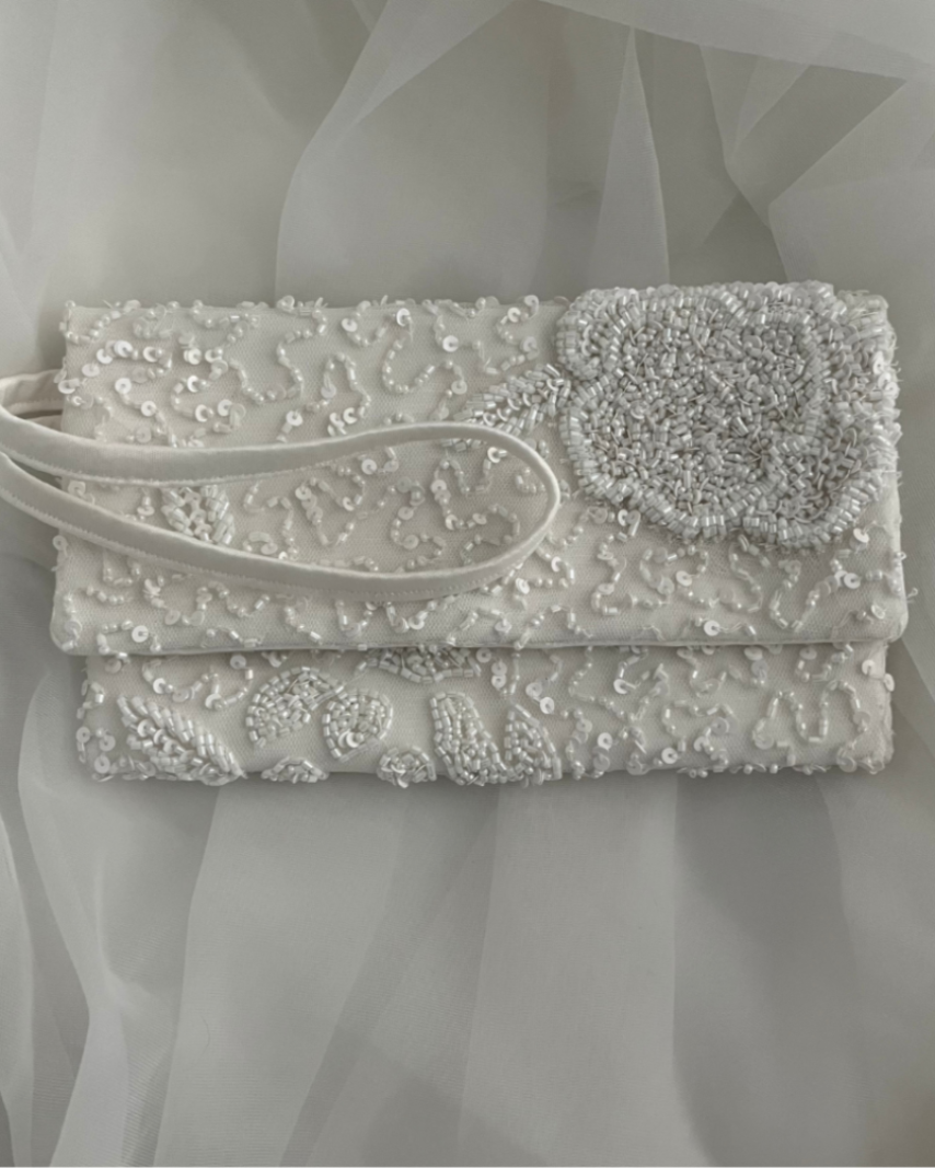 white 8x5 wedding clutch made from repurposed wedding gown. It is heavily beaded and has a flower motif on the flap, and a side strap.