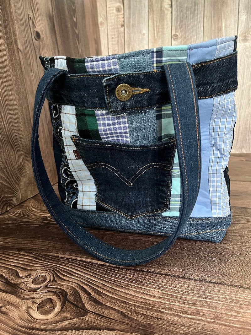 Large denim tote 14x11 made from repurposed jeans and shirts. The bag has quilted stripes of the different shirts in shades of blue. A back pocket of levi jeans are sewn to the front. o