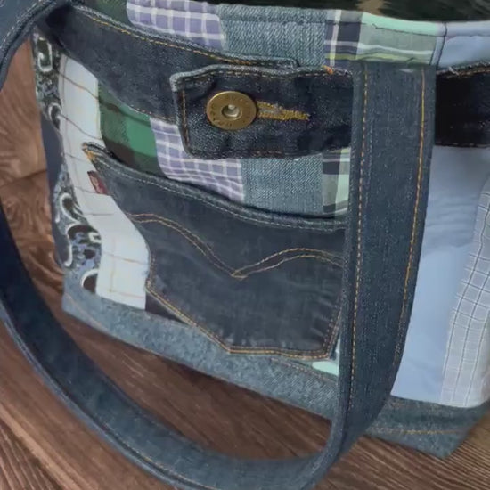 Video of Large denim tote 14x11 made from repurposed jeans and shirts. The bag has quilted stripes of the different shirts in shades of blue. A back pocket of levi jeans are sewn to the front. 