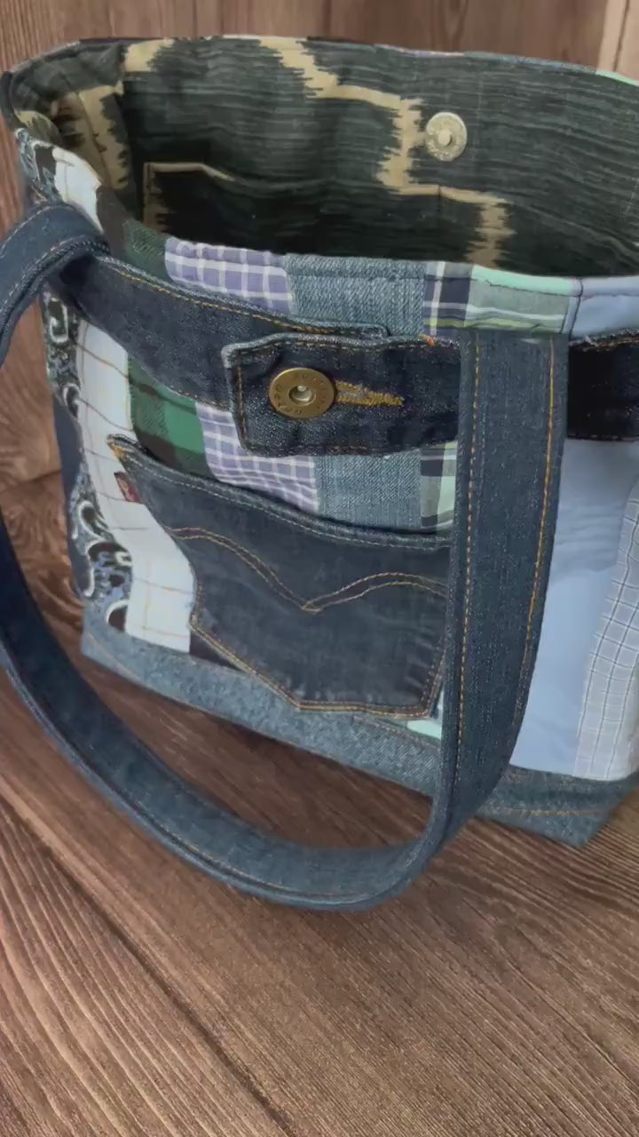 Video of Large denim tote 14x11 made from repurposed jeans and shirts. The bag has quilted stripes of the different shirts in shades of blue. A back pocket of levi jeans are sewn to the front. 